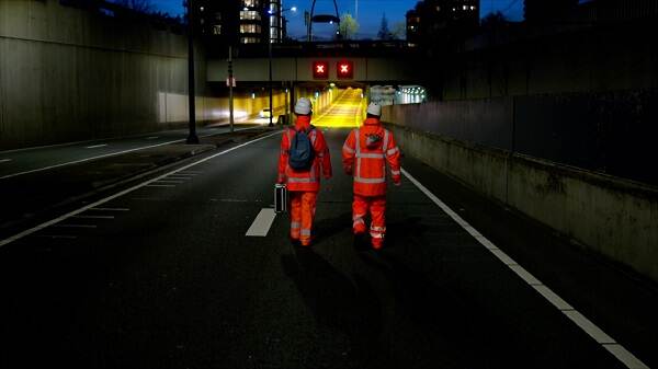 Twee mensen in oranje pak en met een witte helm lopen een tunnel in